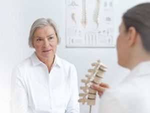 A physical therapist discussing spinal stenosis with a female patient.