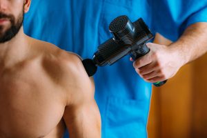 A massage gun being used on a man's shoulder.