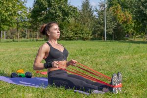 A woman performing seated resistance band rows in the park.
