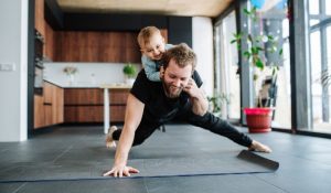 A man doing physical therapy exercises at home while playing with his young toddler.