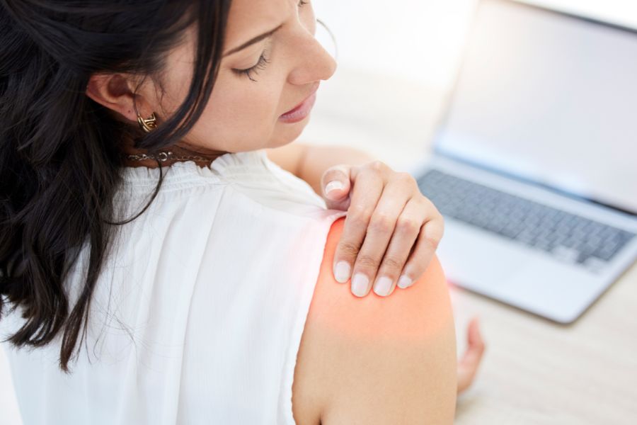 A woman experiencing shoulder pain from poor posture on the computer.