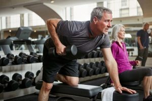 An elderly gentleman lifting dumbbells in a gym.