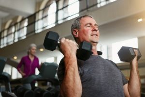 A senior man doing dumbbell curls at the gym.